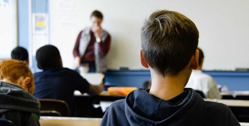 Unga elever i ett klassrum som lyssnar på en lärare som står vid en vit tavla.